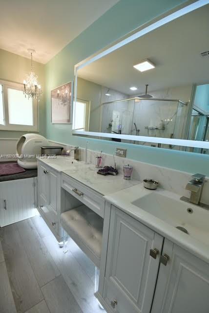 bathroom with a shower with door, a notable chandelier, hardwood / wood-style flooring, and vanity