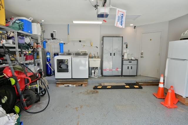 garage with a garage door opener, sink, washing machine and clothes dryer, and white refrigerator