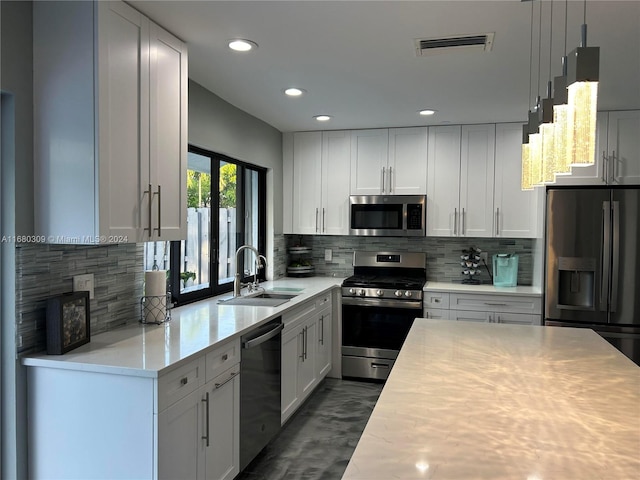 kitchen with tasteful backsplash, sink, white cabinetry, stainless steel appliances, and decorative light fixtures