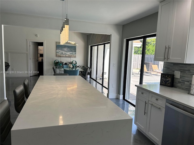 kitchen featuring decorative backsplash, a kitchen island, white cabinetry, stainless steel dishwasher, and decorative light fixtures