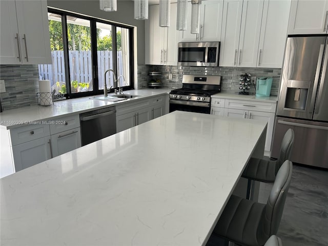 kitchen featuring light stone countertops, sink, stainless steel appliances, white cabinets, and a breakfast bar