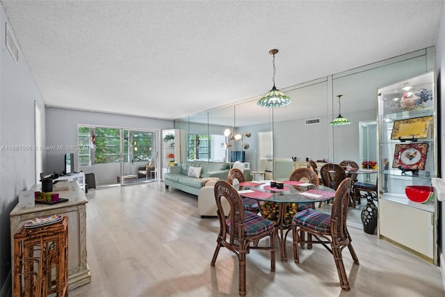 dining area featuring a textured ceiling, light hardwood / wood-style flooring, and an inviting chandelier