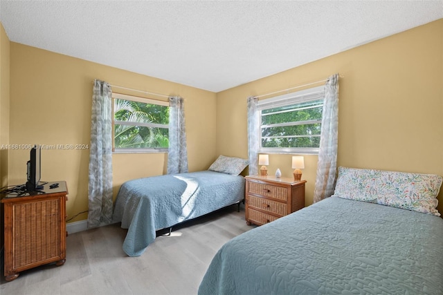 bedroom featuring light hardwood / wood-style floors, a textured ceiling, and multiple windows