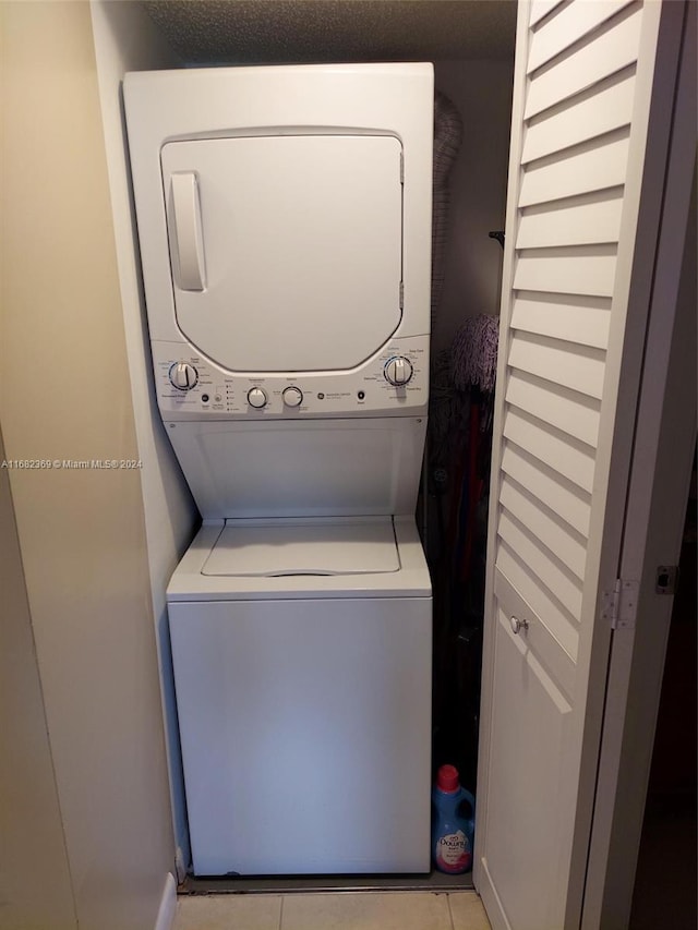 clothes washing area featuring a textured ceiling, light tile patterned floors, and stacked washer and clothes dryer