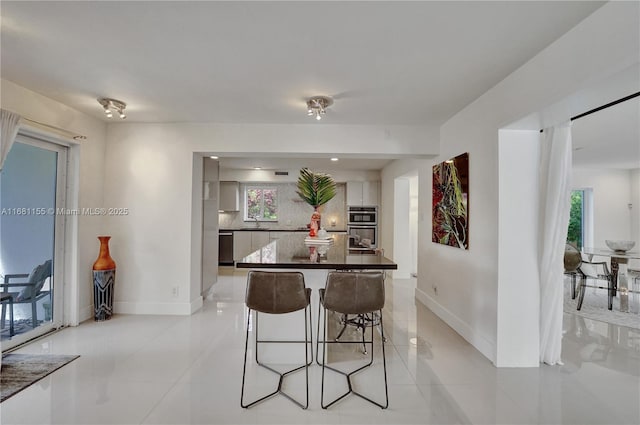 kitchen featuring a breakfast bar, a center island, tasteful backsplash, dark countertops, and baseboards