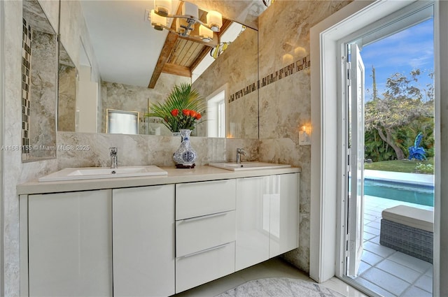 full bath with double vanity, beam ceiling, a sink, and tile walls