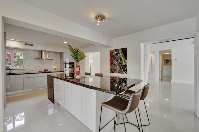 kitchen with a large island, visible vents, stainless steel double oven, modern cabinets, and wall chimney exhaust hood