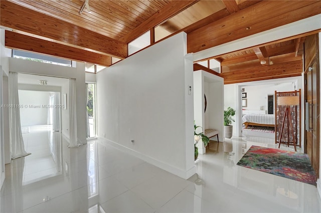 hallway featuring wooden ceiling, tile patterned flooring, baseboards, and beam ceiling