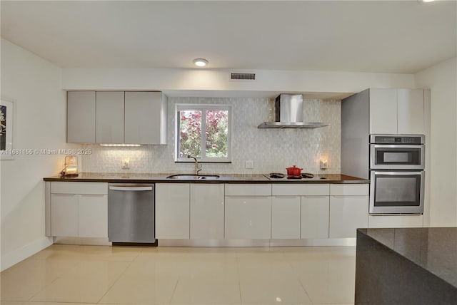 kitchen featuring dark countertops, visible vents, appliances with stainless steel finishes, a sink, and wall chimney range hood