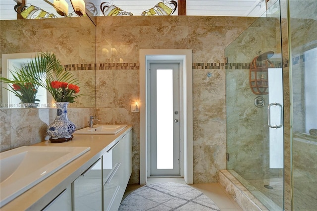 full bathroom featuring double vanity, a stall shower, tile walls, and a sink