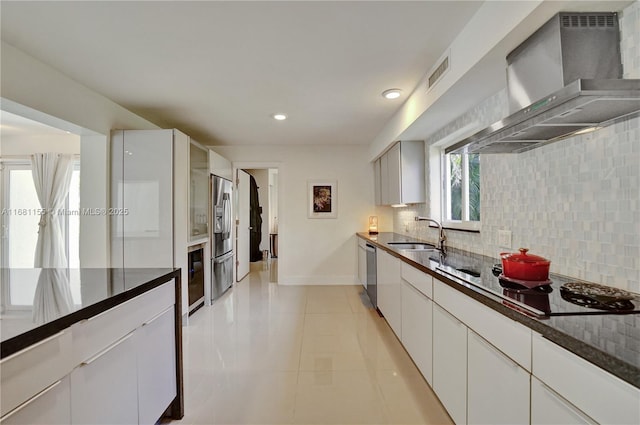 kitchen with wall chimney exhaust hood, tasteful backsplash, appliances with stainless steel finishes, a sink, and baseboards