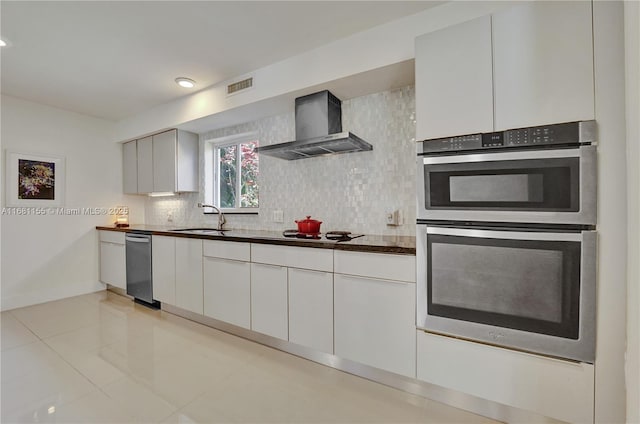 kitchen with visible vents, dark countertops, stainless steel double oven, wall chimney range hood, and backsplash