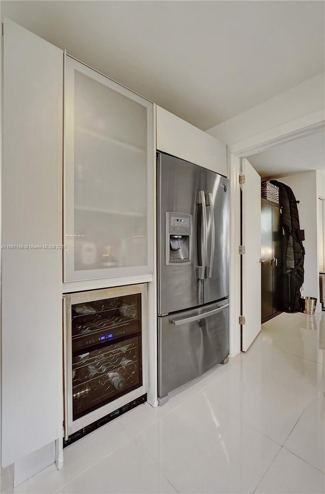 kitchen with beverage cooler, tile patterned flooring, stainless steel fridge, and white cabinetry