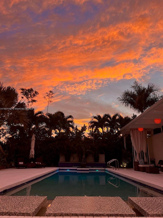 pool at dusk with an outdoor pool and a patio