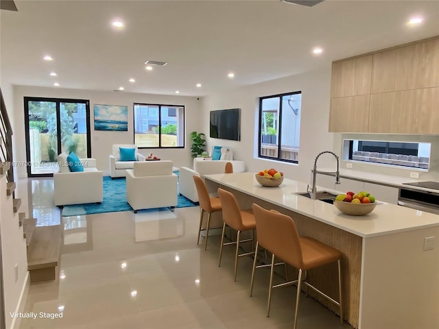 kitchen with a kitchen breakfast bar, black electric stovetop, a kitchen island with sink, sink, and light tile patterned floors