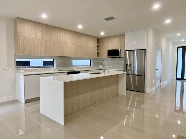 kitchen with sink, light brown cabinets, a kitchen island with sink, light tile patterned floors, and appliances with stainless steel finishes