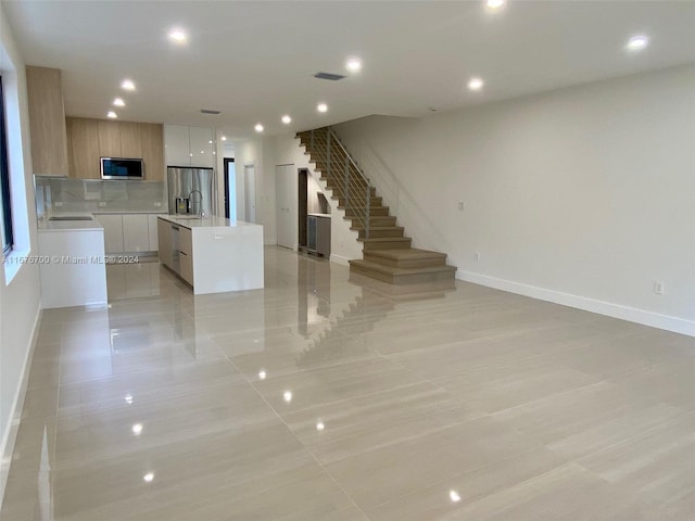 kitchen with light brown cabinets, sink, decorative backsplash, a kitchen island, and appliances with stainless steel finishes