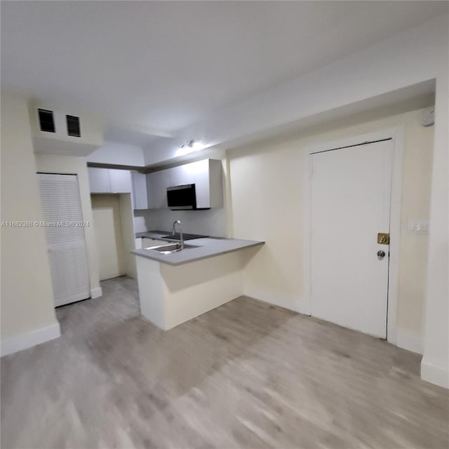 kitchen with light hardwood / wood-style floors, sink, kitchen peninsula, and white cabinets