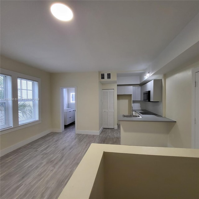 kitchen with light wood-type flooring, sink, kitchen peninsula, and gray cabinets