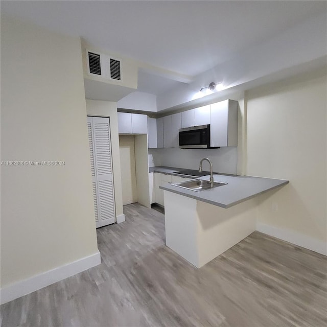 kitchen featuring sink, light hardwood / wood-style flooring, kitchen peninsula, and white cabinetry