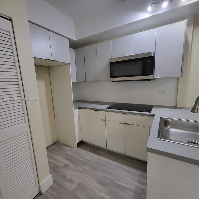 kitchen featuring light hardwood / wood-style flooring, white cabinetry, sink, and black cooktop