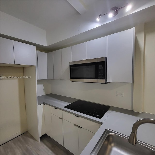 kitchen with sink, black electric stovetop, light hardwood / wood-style flooring, and white cabinets