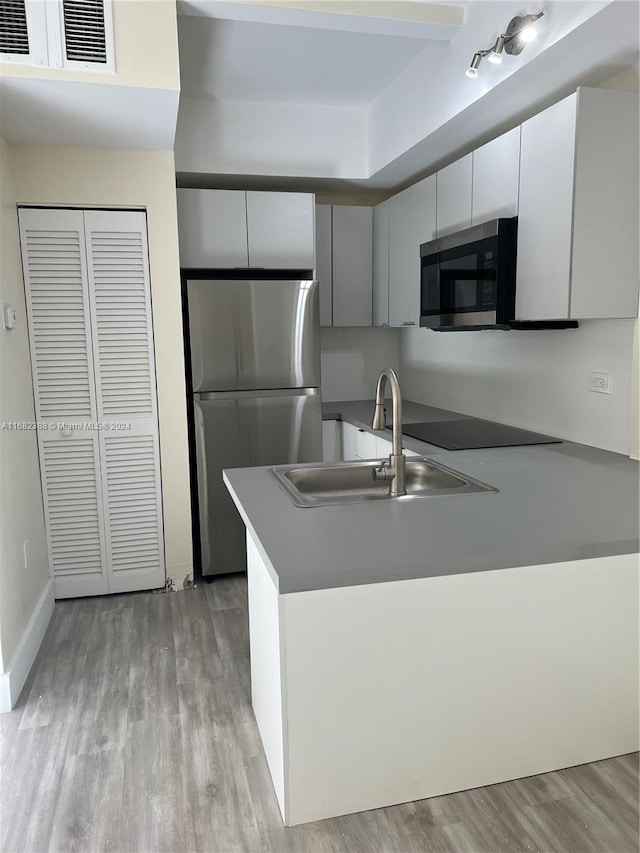 kitchen with kitchen peninsula, stainless steel appliances, sink, white cabinets, and light hardwood / wood-style floors