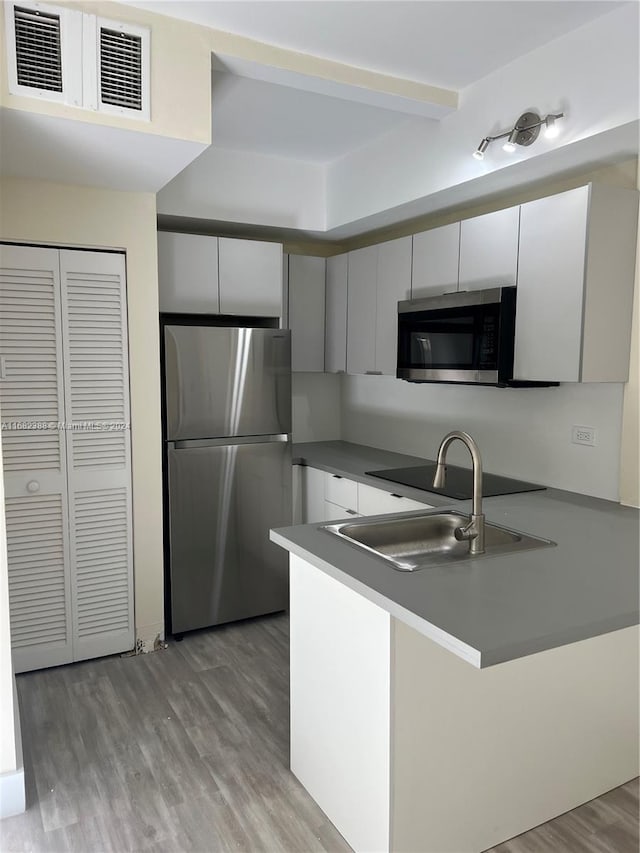 kitchen featuring appliances with stainless steel finishes, sink, kitchen peninsula, light hardwood / wood-style floors, and white cabinets