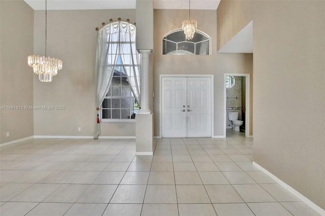 tiled entryway featuring a towering ceiling, an inviting chandelier, and ornate columns