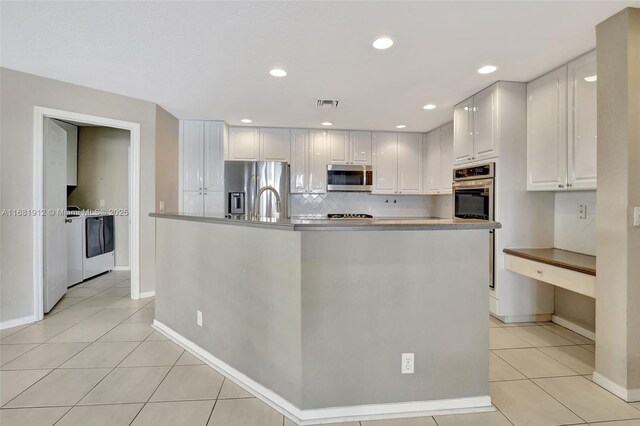 kitchen featuring a kitchen island with sink, washer and dryer, appliances with stainless steel finishes, light tile patterned flooring, and white cabinetry