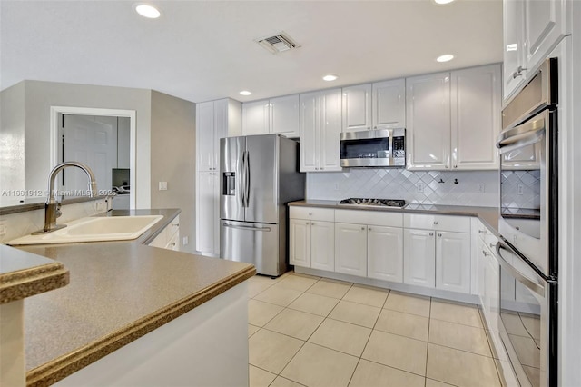 kitchen with backsplash, sink, light tile patterned floors, white cabinetry, and stainless steel appliances