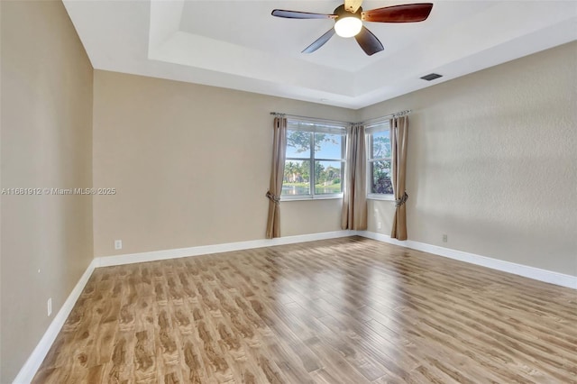 unfurnished room featuring a tray ceiling, ceiling fan, and light wood-type flooring