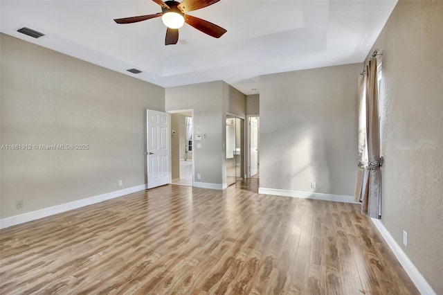 spare room with a tray ceiling, ceiling fan, and light hardwood / wood-style floors