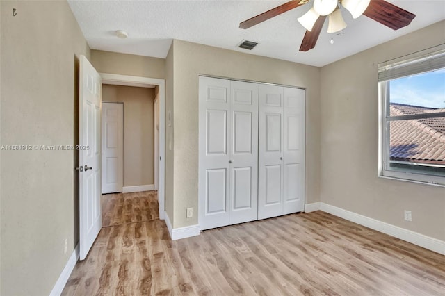 unfurnished bedroom with ceiling fan, a closet, light hardwood / wood-style floors, and a textured ceiling