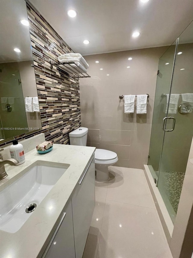 bathroom with tile patterned floors, toilet, a shower with shower door, vanity, and tile walls