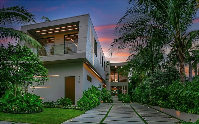 back house at dusk with a yard and a balcony