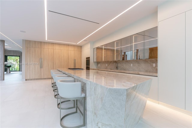 kitchen featuring light stone countertops, backsplash, light tile patterned flooring, and a breakfast bar area