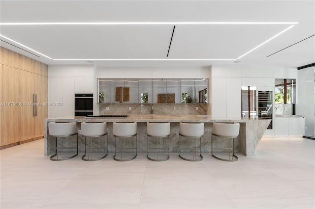 kitchen featuring white cabinetry, decorative backsplash, light stone counters, and a kitchen breakfast bar