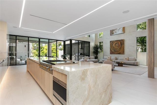 kitchen featuring stainless steel appliances, light stone counters, floor to ceiling windows, light brown cabinetry, and a center island