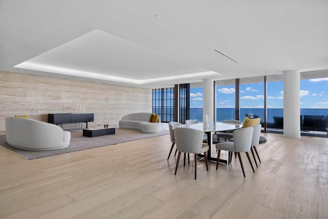 dining area featuring expansive windows, a water view, light wood-type flooring, and a tray ceiling