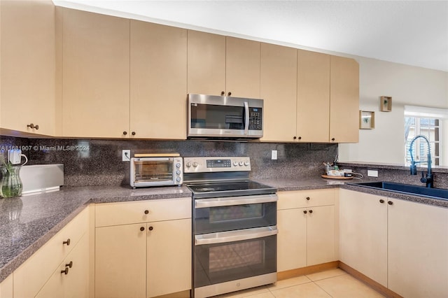 kitchen with decorative backsplash, cream cabinets, appliances with stainless steel finishes, light tile patterned flooring, and sink