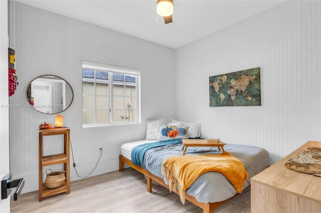 bedroom featuring light hardwood / wood-style floors, wooden walls, and ceiling fan