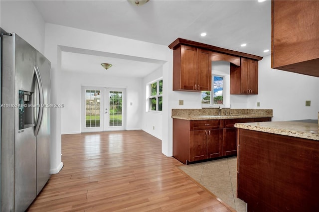 kitchen with recessed lighting, french doors, light stone countertops, light wood finished floors, and stainless steel fridge