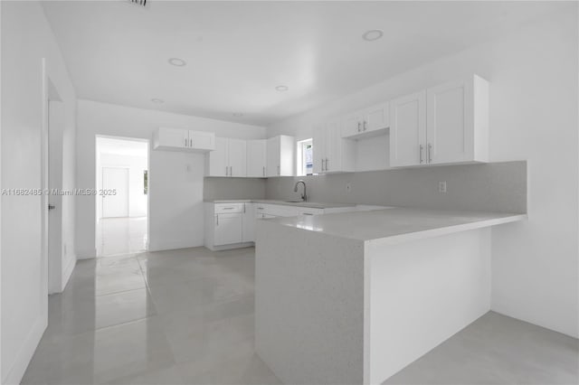 kitchen featuring white cabinets, kitchen peninsula, backsplash, and sink