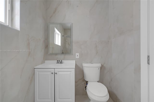 bathroom with toilet, vanity, tile walls, and plenty of natural light