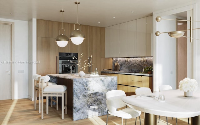 kitchen with light brown cabinets, light hardwood / wood-style flooring, hanging light fixtures, black double oven, and tasteful backsplash