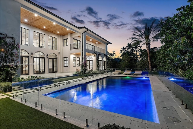 pool at dusk with pool water feature and a patio