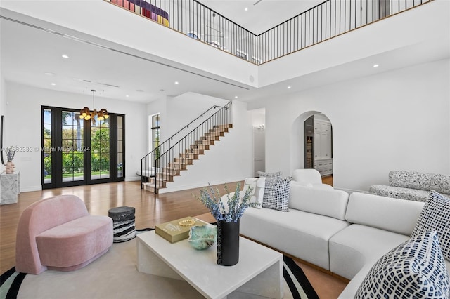 living room with french doors, light hardwood / wood-style floors, a notable chandelier, and a towering ceiling