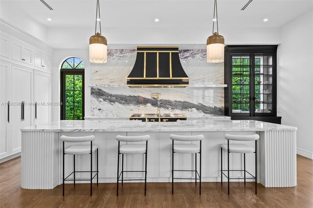 406 Tamarind Dr, Hallandale Beach, FL 33009 - kitchen with range hood, light stone countertops, dark wood-type flooring, white cabinetry, and decorative light fixtures