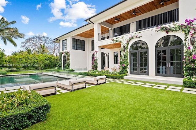 rear view of property featuring french doors, a lawn, and a balcony